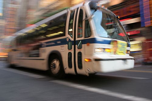 City transit bus driving quickly down a busy urban street with motion blur.