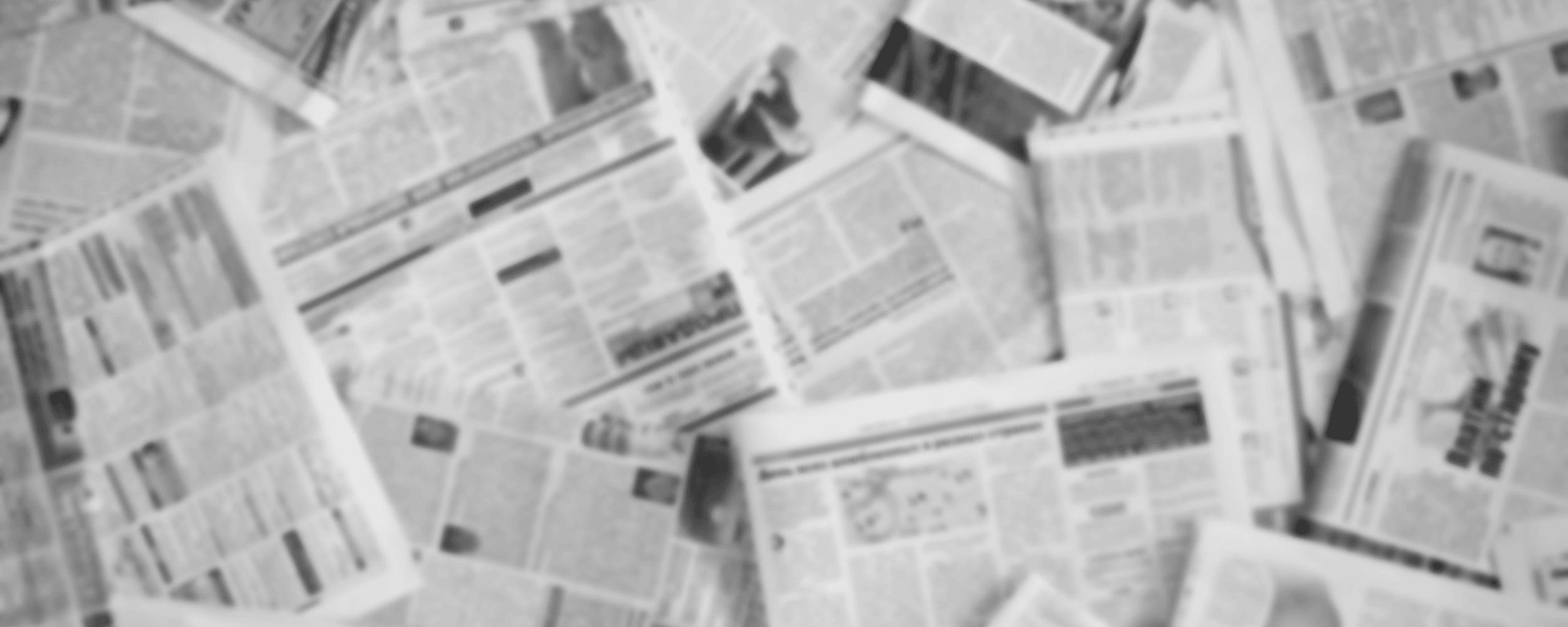 Overhead view of scattered black and white newspapers with visible headlines and articles, creating a textured background.