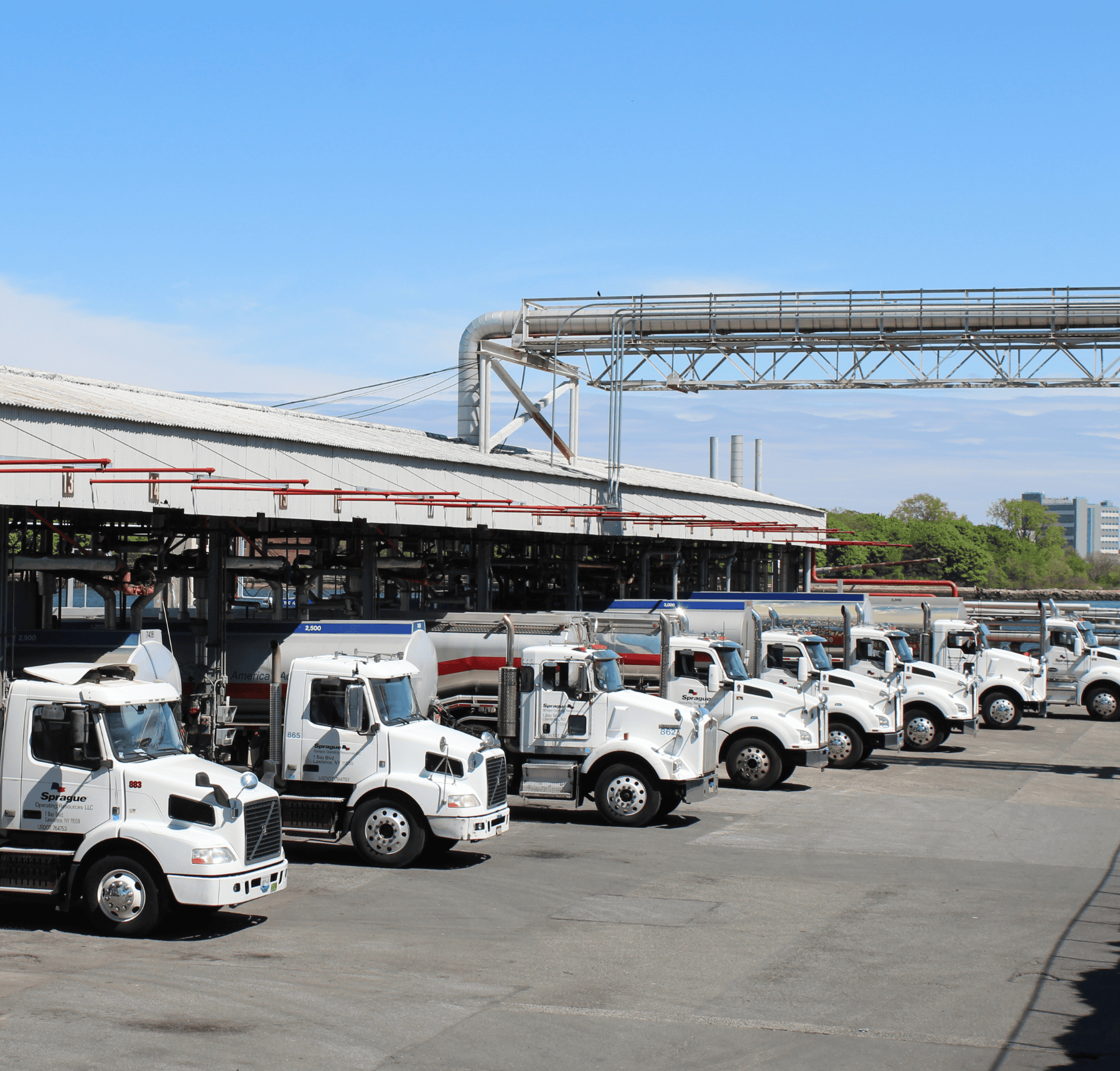 Fleet of Sprague Energy fuel trucks lined up at a distribution terminal, ready for dispatch.