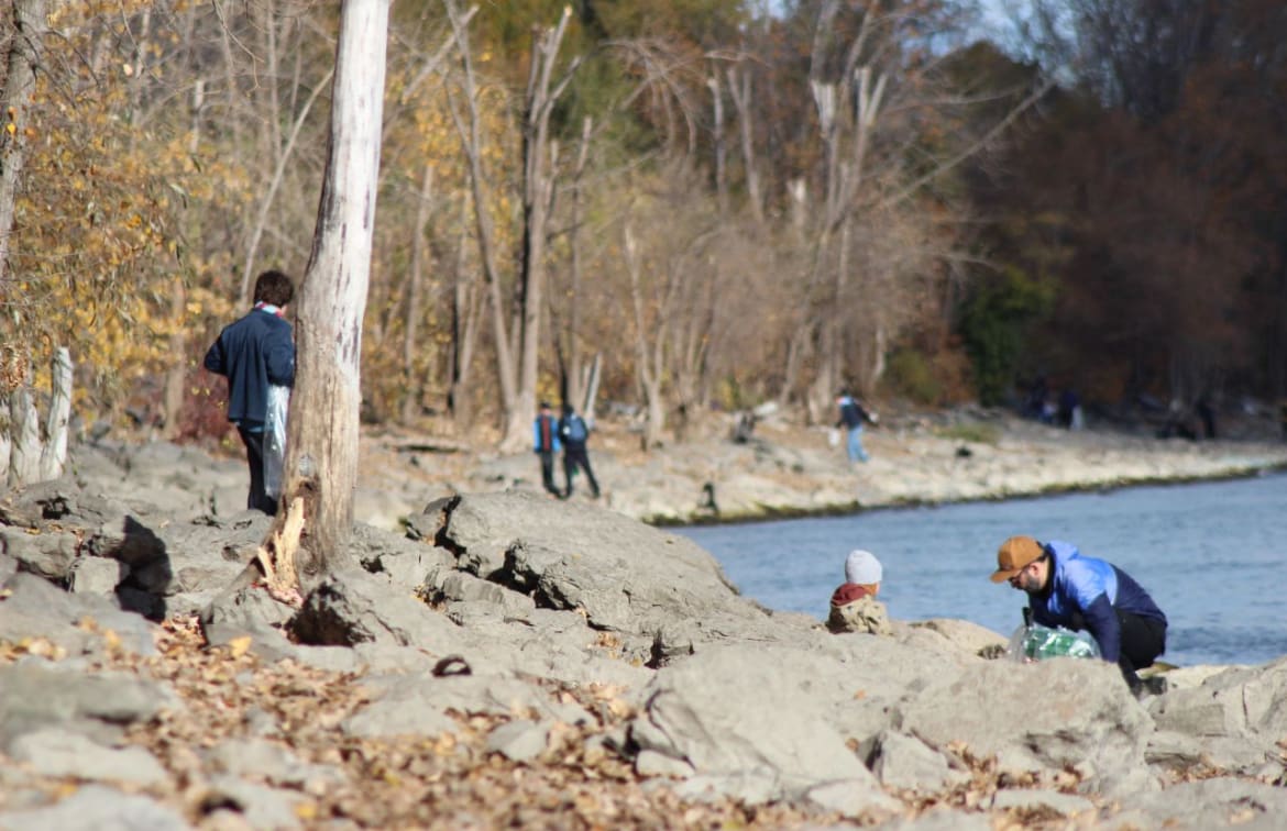 Volunteers picking up litter along a rocky riverside in autumn, participating in a community cleanup event.