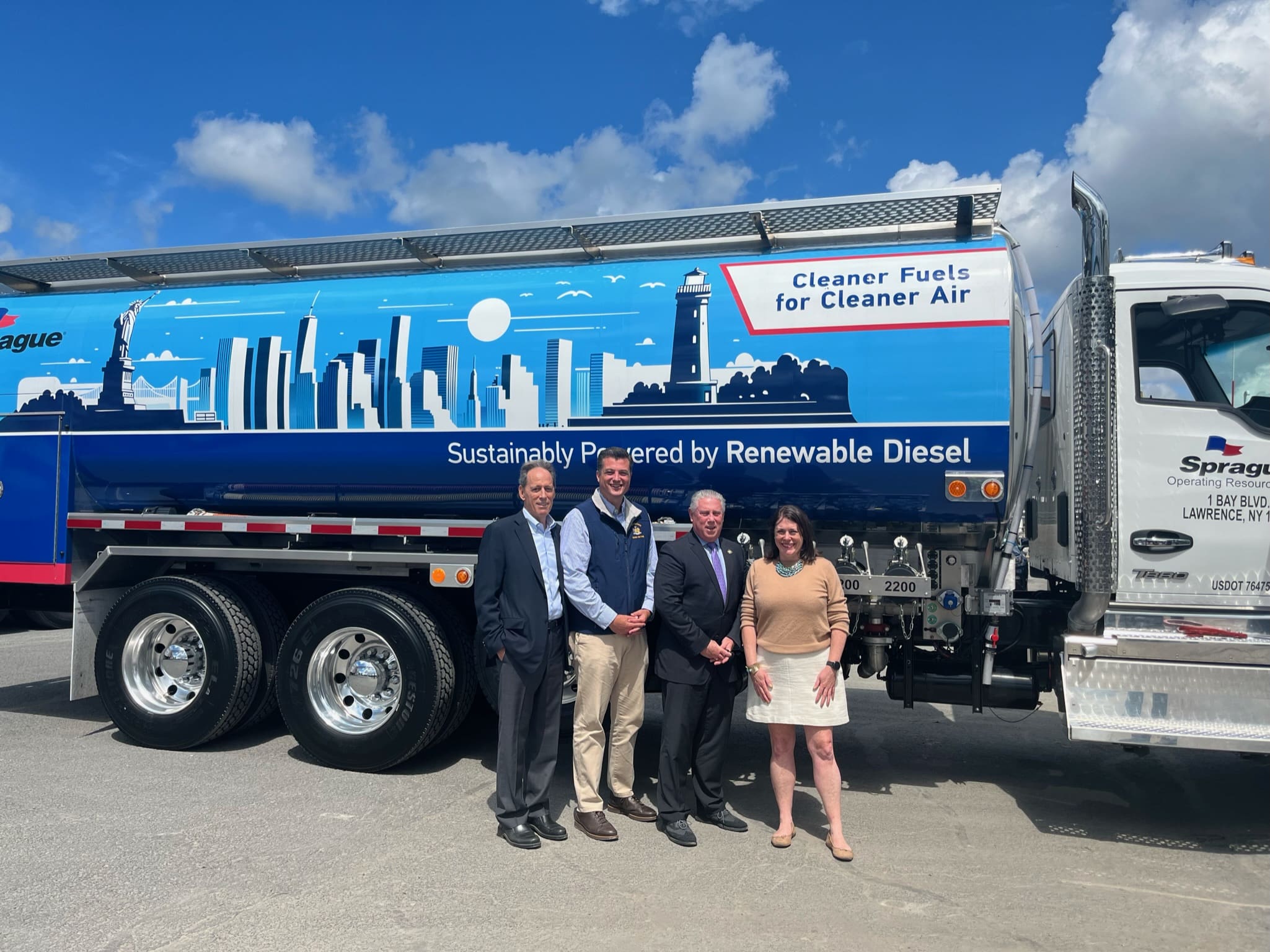 Four individuals stand in front of a Sprague Energy renewable diesel truck featuring skyline artwork and the slogan 'Cleaner Fuels for Cleaner Air,' promoting clean fuel initiatives in New York.